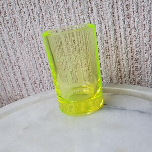 May include: A bright yellow glass shot glass. The glass is clear and has a rounded bottom.