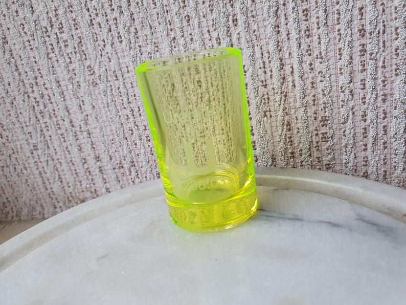 May include: A bright yellow glass shot glass. The glass is clear and has a rounded bottom.