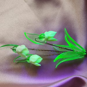 May include: A bouquet of green glass lily of the valley flowers with white blossoms. The flowers are attached to a wire stem.