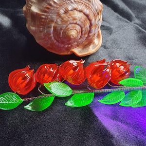 Könnte beinhalten: Ein Glasblumenstiel mit roten Glasblumen und grünen Glasblättern. Die Blumen sind glockenförmig und die Blätter sind lang und schmal.