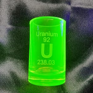 Può includere: Un bicchierino da shot in vetro verde con la scritta "Uranium 92 U 238.03" incisa sul lato.