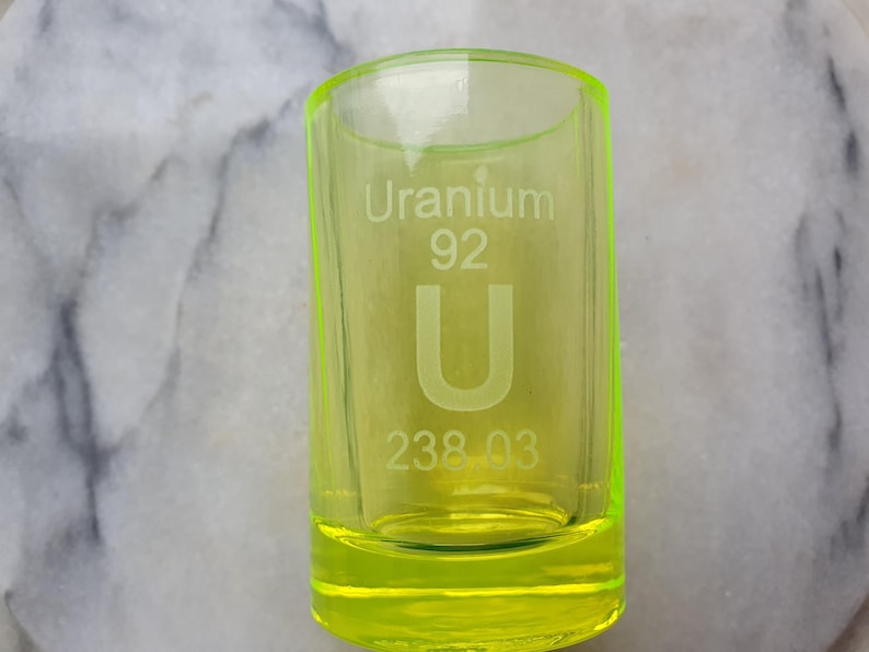 May include: A bright yellow shot glass with the text "Uranium 92 U 238.03" etched on the side.