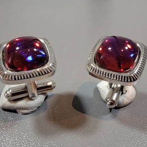 May include: A pair of silver cufflinks with square red and purple iridescent glass stones.