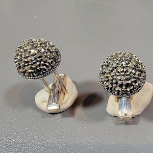 May include: A pair of silver cufflinks with round, black marcasite stones set in a silver bezel. The cufflinks are on a white surface.