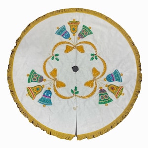 May include: White Christmas tree skirt with a gold fringe border. The skirt features a design of colorful bells, gold ribbons, and holly leaves. The bells are in shades of blue, green, and yellow.