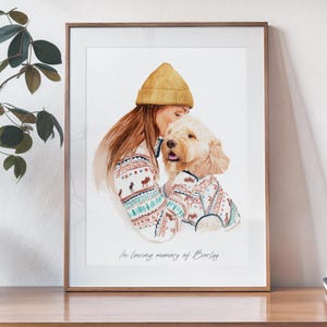 Könnte beinhalten: Aquarellporträt einer Person und eines Hundes, beide in passenden Pullovern mit festlichem Muster. Die Person trägt eine gelbe Mütze. Der Text "In loving memory of Barley" steht unten auf dem Druck. Das Kunstwerk ist in einem braunen Holzrahmen gerahmt.