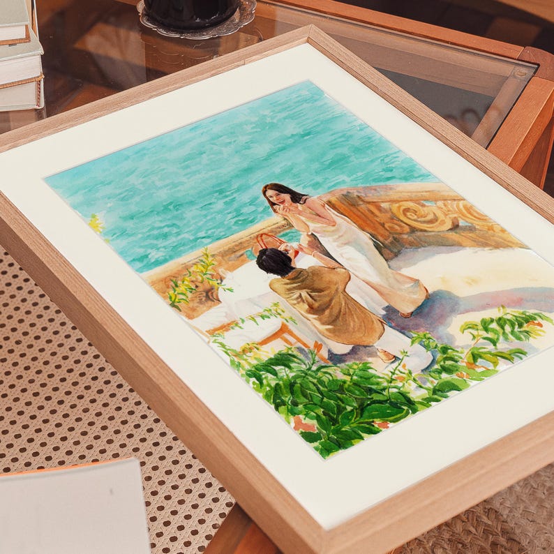 May include: Watercolor painting in a light wood frame. The artwork depicts a couple on a balcony overlooking the sea. The woman is wearing a white dress, and the man is kneeling. Green foliage and a turquoise sea are visible.