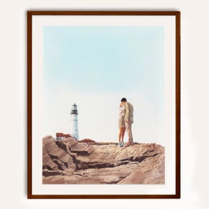 May include: A framed watercolour print shows a couple embracing on a rocky cliff with a lighthouse in the background. The lighthouse is white with a black top, and the sky is pale blue. The rocks are brown and tan.