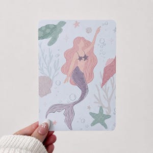 May include: A rectangular art print featuring a central mermaid with long pink hair and a purple tail, surrounded by a green sea turtle, a green starfish, pink seashells, coral branches, and small bubbles on a light blue background.