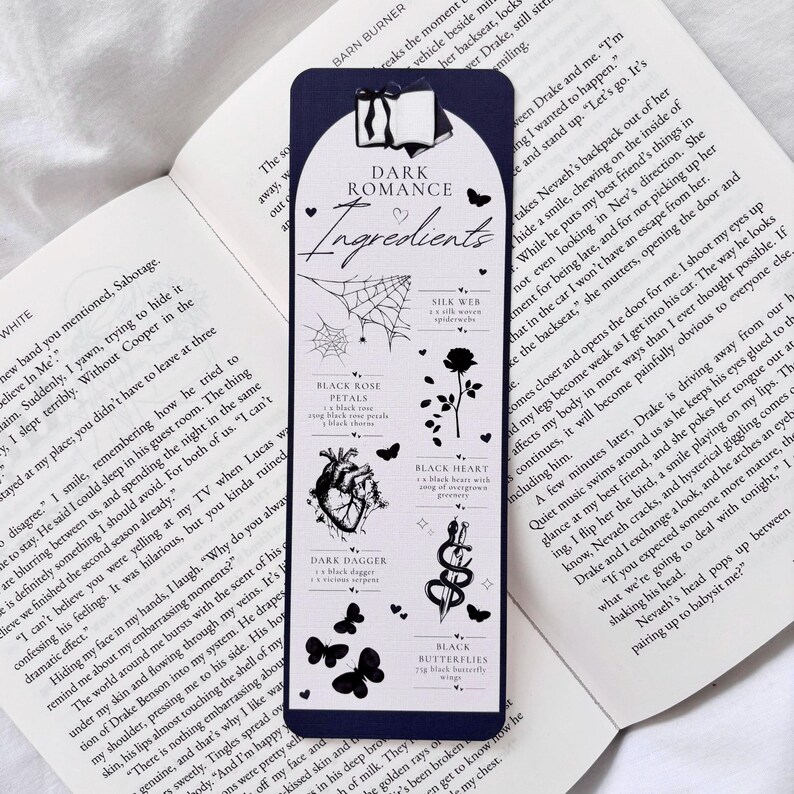 May include: A dark blue bookmark with the text "Dark Romance Ingredients" and black and white illustrations of a spider web, a black rose, a heart, a dagger, a snake, and butterflies.