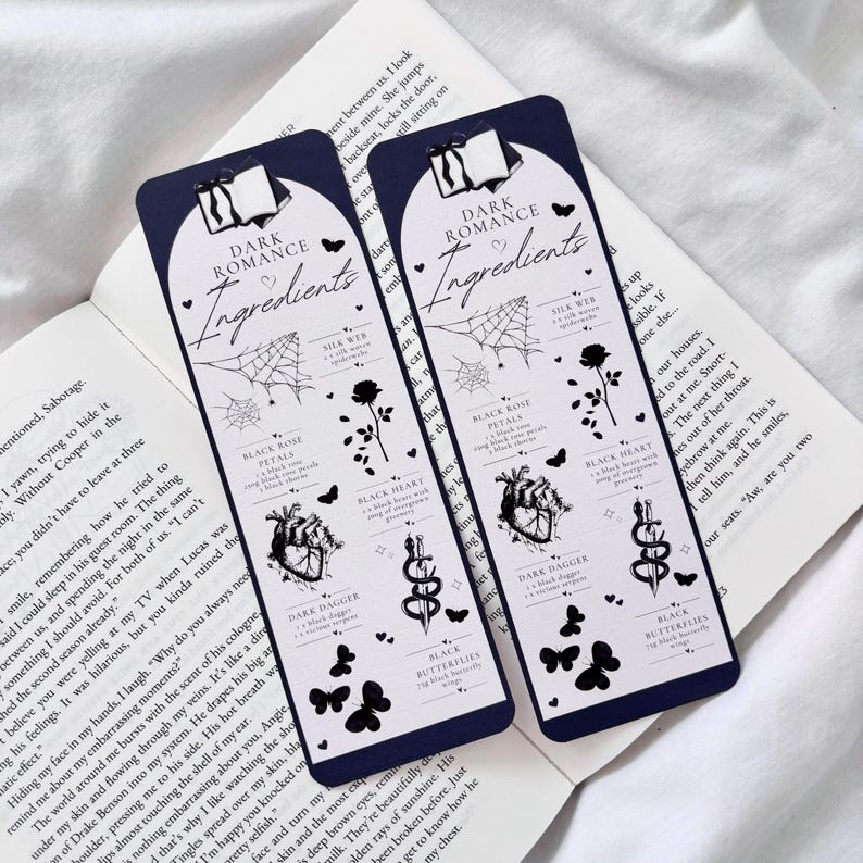 May include: Two black and white bookmark designs with a dark blue background. The bookmarks feature a variety of dark romance themed illustrations, including a black heart, a black rose, a dagger, a snake, a spider web, and butterflies. The text on the bookmarks reads "Dark Romance Ingredients".