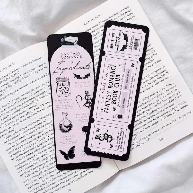 May include: A black and pink bookmark with a fantasy romance theme. The bookmark features a ticket with the text "Official Member of the Fantasy Romance Book Club" and a list of ingredients for a fantasy romance potion, including a black heart and dagger, a bottle of moonlight, and a black rose.