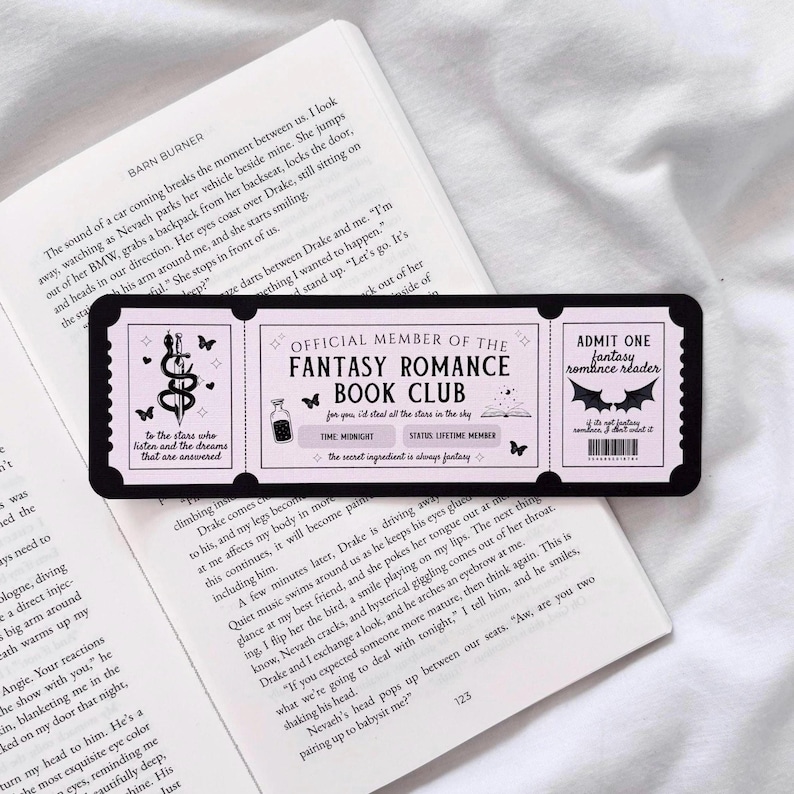 May include: A pink and black bookmark with a ticket design. The bookmark features a black and white illustration of a bat and the text "Admit One Fantasy Romance Reader". The bookmark also features a black and white illustration of a potion bottle and the text "Official Member of the Fantasy Romance Book Club".