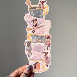 May include: A sticker showing a stack of teacups, each with a witch. The witches are in different poses, some on brooms, others relaxing. The teacups are pastel-coloured with celestial and floral designs. The sticker is a whimsical design.