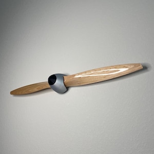 May include: A wooden airplane propeller with a silver metal base. The propeller is mounted on a wall.