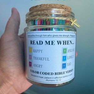 May include: A glass jar with a cork lid and a gold cross charm. The jar contains colorful paper strips and a label that reads "READ ME WHEN..." with prompts for different emotions. The text also includes Bible verses.