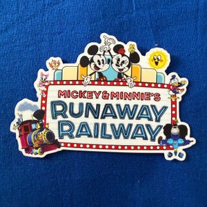 Könnte beinhalten: Ein gestanzter Aufkleber mit Mickey und Minnie Mouse über einem Schild mit der Aufschrift Mickey & Minnie's Runaway Railway in blauer und roter Schrift. Das Design zeigt einen bunten Dampfzug, eine gelbe Sonne und verschiedene Figuren.