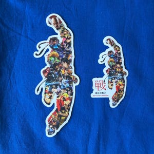 Könnte beinhalten: Zwei gestanzte Aufkleber auf blauem Hintergrund. Die Aufkleber haben die Form einer stilisierten Hand, gefüllt mit einer Collage farbenfroher Anime-Charaktere. Ein Aufkleber hat japanischen Text mit der Aufschrift "Battle of Horizons".