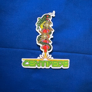 May include: A green, red, and yellow sticker with a cartoon centipede and the word "CENTIPEDE" in yellow letters.
