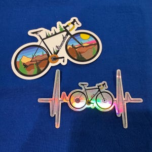Pegatinas mate/holográficas troqueladas con arte ciclista y latidos del corazón.