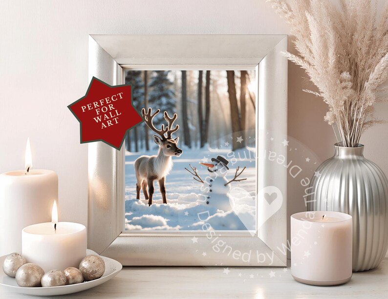May include: A framed winter scene featuring a reindeer and snowman in a snowy forest. The image is in a silver frame, with a red star-shaped sticker that says "PERFECT FOR WALL ART". The scene is flanked by lit candles and a decorative vase.