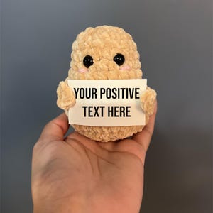 May include: A crocheted plush toy shaped like a cell holding a sign that says "YOUR POSITIVE TEXT HERE".