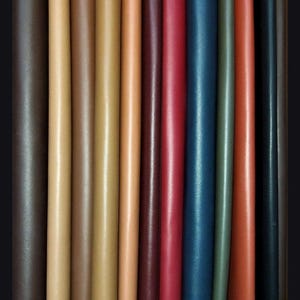 May include: A collection of 12 leather strips in various colors, including brown, tan, red, blue, and green. The strips are arranged side by side, showcasing the different shades and textures of the leather.