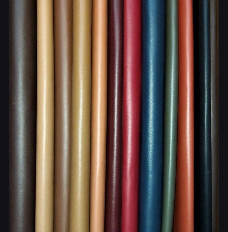 May include: A collection of 12 leather strips in various colors, including brown, tan, red, blue, and green. The strips are arranged side by side, showcasing the different shades and textures of the leather.