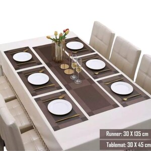 May include: A dining table set with a white tablecloth, brown runner (30 x 135 cm), and matching placemats (30 x 45 cm). Each place setting includes a white plate and gold-coloured cutlery. The table is set for a formal dinner.