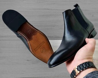 May include: Black leather Chelsea boots with elastic side panels and a brown leather sole. The sole has the text "Sole Survivors" printed on it.