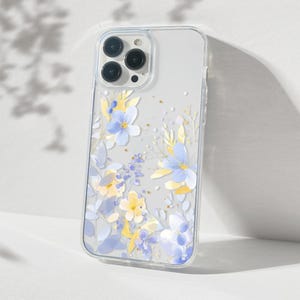 Puede incluir: Una funda transparente para teléfono con un diseño floral con flores azules y amarillas. La funda está diseñada para un iPhone 13 Pro Max.