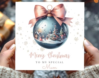 May include: A Christmas card featuring a blue ornament with a winter village scene and a pink bow. The card reads "Merry Christmas To My Special Mum" in a delicate script, with snowflakes scattered around.