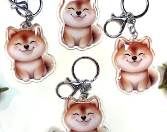 Op de afbeelding: Vier transparante acryl sleutelhangers met een cartoon Shiba Inu hond met een glimlachend gezicht. Elke sleutelhanger heeft een zilveren metalen ring en een zilveren metalen sluiting.