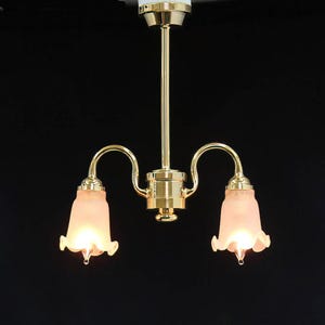 Op de afbeelding: Een kroonluchter met twee lampen, voorzien van een centrale stang en gebogen armen met een gepolijste messing afwerking. Het armatuur bevat twee klokvormige, matroze glazen kappen met geschulpte randen die warm licht uitstralen.