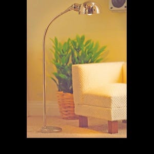 Op de afbeelding: Een zilverkleurige vloerlamp met een gebogen hals en een koepelvormige kap. De lamp heeft een ronde voet en een verstelbare kop. Het getal 5727 wordt weergegeven in de rechterbenedenhoek van de afbeelding, waarop de lamp staand te zien is.