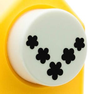 May include: A white craft punch with a yellow base. The punch has five black flower shapes on the cutting surface.