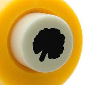 Puede incluir: Un punzón artesanal amarillo y blanco con una silueta de un árbol. El punzón está diseñado para crear un pequeño agujero en forma de árbol en el papel.