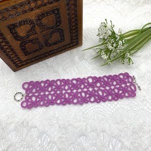 May include: A purple crocheted bracelet with a delicate floral pattern and silver clasps.