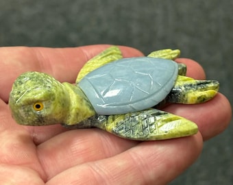 May include: A carved stone turtle figurine. The turtle has a light blue shell and a green and yellow body. The turtle's head has a yellow eye. The figurine is a decorative item.