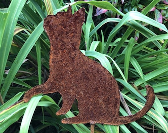 May include: A rusty metal cat silhouette garden stake. The cat is sitting with its tail curled around its body. The stake is brown and has a rustic look.
