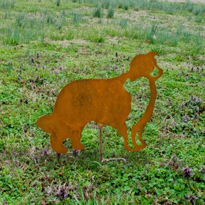 May include: A rusty metal silhouette of a dog standing in a grassy field. The dog is facing to the left and has its head tilted down.