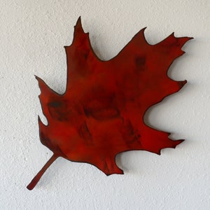 May include: A large, red metal leaf with a textured surface. The leaf is shaped like a maple leaf and has a stem.