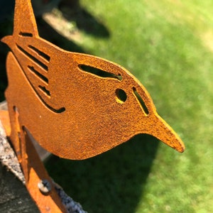 May include: A rusty metal wren silhouette mounted on a wooden post. The wren is facing right and has a detailed design with a textured surface.