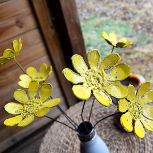May include: A bouquet of yellow metal flowers in a gray vase. The flowers are made of recycled metal and have a textured finish.