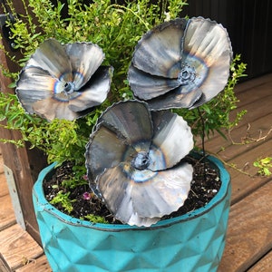 May include: A turquoise planter with a geometric pattern holds three metal poppy flowers. The flowers are made of metal and have a burnished finish. The flowers are arranged in a cluster in the center of the planter.