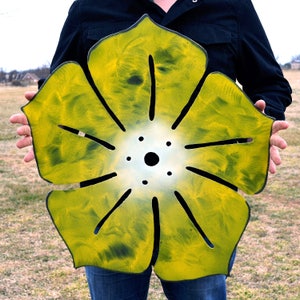May include: A large metal flower with a yellow and green paint finish. The flower has a circular center with a white background and a black circle in the middle.