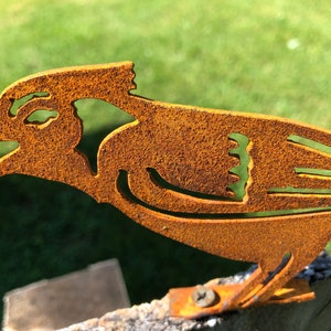 May include: A rusty metal bird sculpture with a detailed design. The bird is facing right and has its beak open. The sculpture is mounted on a wooden post.