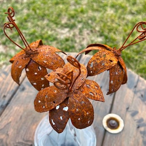 May include: Three rusty metal flowers with wire stems. The flowers are made of thin metal and have a rustic, aged look.