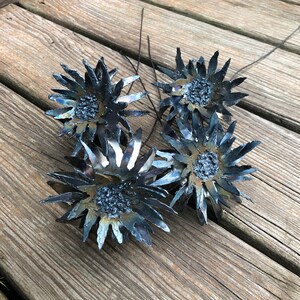 Op de afbeelding: Een boeket van vijf metalen zonnebloemen in zwart en blauwe tinten. De zonnebloemen zijn gemaakt van metaal en hebben een rustieke, industri&euml;le uitstraling.