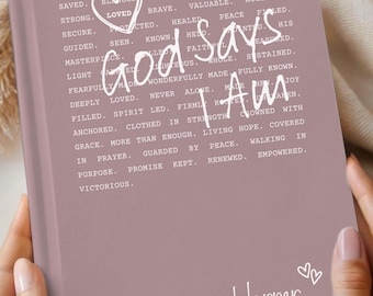 May include: A rosewood-coloured journal with the words "God says I Am" in white script. The journal has a heart graphic and the name "Harper" at the bottom. The journal is held in two hands.
